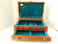 Front view of open jewelry box showing top tier with 10 small compartments, second tier with 3 compartments and ring roll, and bottom drawer opened with divider, emerald green velvet lining visible.