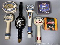 Photo showing six beer tap handles, including Creemore Springs Premium Lager (2), Creemore Springs urBock, Waterloo Dark, and one unlabeled black wooden handle. Also includes assorted beer coasters.