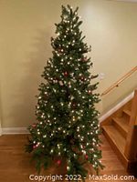 Full assembled Christmas tree about 7 feet tall, lit with white and red lights, positioned near stairs.