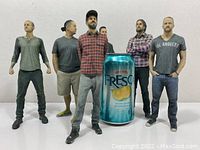 Six figures arranged behind a soda can for scale