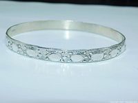 Silver tone bangle bracelet embossed with turtle patterns viewed at an angle showing the bracelet thickness and detail.