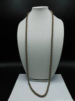 Full view of the necklace displayed on a white bust showing the length and color of the pearl strand.