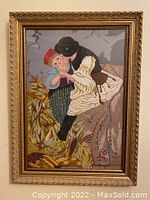 Full view of framed vintage needlepoint artwork depicting an embracing couple, possibly European folk dancers, in colorful traditional dress with plants in the background