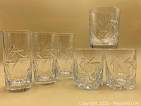 Set of six vintage pinwheel crystal highball and whiskey glasses showing front view of glasses lined up with one whiskey glass elevated.