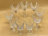 Nine vintage pinwheel crystal stemware glasses arranged in a circular fashion on a wooden surface, showing the three different types grouped together to illustrate the complete set.
