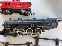 Close-up image of black American Flyer engine locomotive number 282 with red caboose and other cars visible.