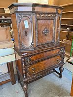 Front and side view of ornate antique wood carved dresser showing detailed carvings, door panels, and metal hardware.