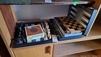 Wooden chess set in an open cigar box alongside a closed blue-gray game case with boards inside.