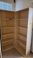 Two light wood grain bookcases placed in a corner showing multiple shelves.