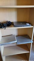 Photo of three laptops on shelves: one Dell Inspiron, one other Dell laptop, one Acer laptop, with charging cords beside them.