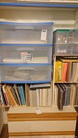 View of shelving unit with large collection of art paper pads and loose sheets, and plastic storage totes containing art supplies.