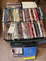 Box containing about 60 assorted DVD movies and documentaries in cases, stacked tightly including various film titles.