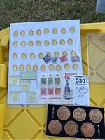 Photo showing sheet of gold-colored space medallions, assorted vintage stamps, and postcard with a bottle image labeled Tuborg