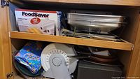 FoodSaver vacuum sealer base, rolls of bags, and other appliances in cabinet