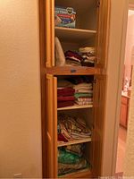 Cabinet with folded towels, linens, sheets, blankets stacked on shelves.