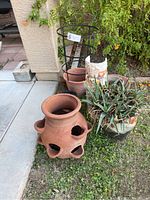 Photo showing large terra cotta strawberry pot, aloe-containing glazed ceramic pot with wave design, tomato cage holder, and smaller terra cotta pot in background