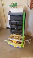 Overall view of the Rubbermaid style cabinet with plastic drawers, items within drawers partially visible, yellow tray at base with hand tools and supplies
