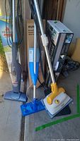 Photo showing Bissell Featherweight vacuum, blue and white Clorox mop, and yellow and white Haan floor sanitizer standing together.