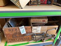 Photo showing wooden Cutty Sark Scotch Whisky box holding various vintage hand tools, some loose on shelf including wrenches and gardening tools.