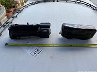 Top down photo showing two black toy train cars (locomotive and tender) alongside a yellow tape measure showing approximate length in inches.