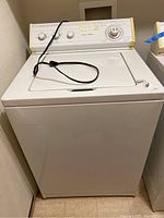 Front view of the white Whirlpool top load washing machine showing body and top with electrical cord on top.