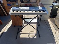 Front view of Yamaha PSR-275 keyboard on black X-style metal stand showing entire keyboard and stand.