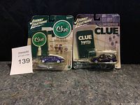Photo shows two Johnny Lightning diecast Clue cars in original blister packaging with visible wear.