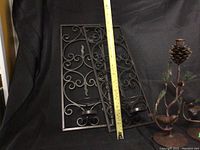 Wall hanging metal candle holders displayed on black cloth background with a measuring tape showing length