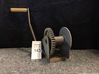 Boat winch with handle and gear mounted on base, photographed against black background.