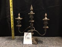 Front view of the electroplated 3-arm candelabra showing metal arms, candle holders, and ornate base with measuring tape for scale.