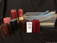 Lot of assorted candles arranged with star-shaped, rectangular, square pillar candles, bundles of red taper candles and loose blue and white taper candles in plastic container.
