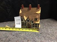 Front view of ceramic Christmas village house with snow accents and chimneys, showing scale measurement approximately 7 inches wide.