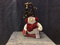 Front view of the Christmas snowman decoration showing its red earmuffs, scarf, and brown antlers with bells attached.