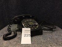 Side view of the vintage black rotary dial desk telephone showing coiled handset cord and metal dial.