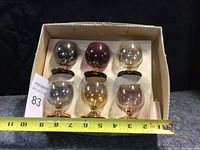 Box containing six vintage glass goblets in various colored bowls and gold-tone bases, with measuring tape showing size