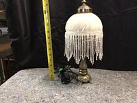 Side view of vintage table lamp with beaded fringe and measuring tape showing height around 16 inches