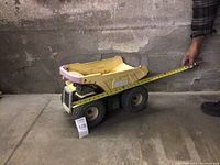 Large metal Tonka dump truck on concrete floor with measuring tape showing length measurement.