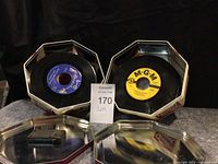 Front view showing two 45 RPM records with labels visible inside two octagonal metal tins.
