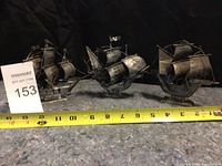 Three metal ship models arranged side by side on a textured surface with measuring tape indicating length around 12 inches for the largest ship.