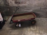 Side view of a red Radio Flyer metal wagon showing the pull handle and visible rust inside the basin.