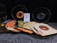Loose 45 RPM vinyl records with visible labels placed near two metal tins.