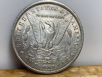 Reverse side of the 1889 American silver dollar showing the eagle with wings spread, clutching arrows and olive branch, surrounded by the inscriptions 'UNITED STATES OF AMERICA', 'In God We Trust', and 'ONE DOLLAR'.