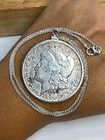 Photo showing 1901 Morgan silver dollar coin pendant front side with Lady Liberty portrait and chain lay on hand.