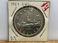 Front side of the 1957 Canadian Silver Dollar coin showing the voyageur design with two men paddling a canoe and the word 'CANADA DOLLAR 1957'. The coin is housed in a white protective cardboard holder with handwritten notes.