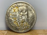 Reverse side of a 1958 Canadian silver dollar coin showing a totem pole design with discoloration spots.