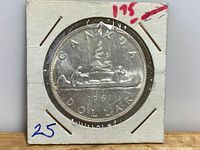 1961 Canadian silver dollar coin showing the canoe design with a man and woman paddling, dated 1961, in protective cardboard holder with handwritten marks.