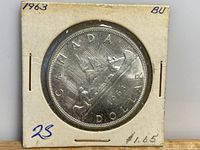 Front view of the 1963 Canadian silver dollar coin in a paper flip holder showing details of the Voyageur design with inscriptions visible.