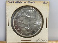 Front side of the 1963 Canadian silver dollar showing the Arrow Head design with the year marked, held in a protective cardboard case.