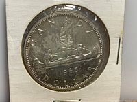 Reverse side of the 1965 Canadian silver dollar showing the voyageur and canoe design with the year 1965.