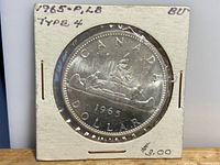 1965 Canadian Silver Dollar, Type 4, P.L.B. initials, in cardboard holder marked BU, front side showing canoe design with two men paddling, Canadian pine trees, year 1965, and text CANADA DOLLAR.